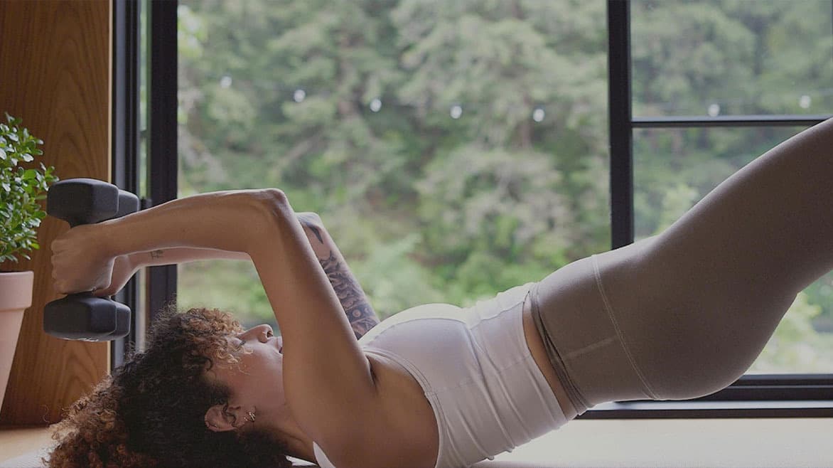 A barre3 client doing a weighted bridge beside a large window