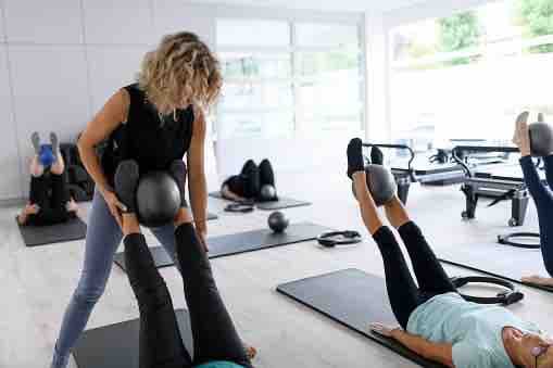 A Pilates instructor guiding a client through a leg exercise with a small ball
